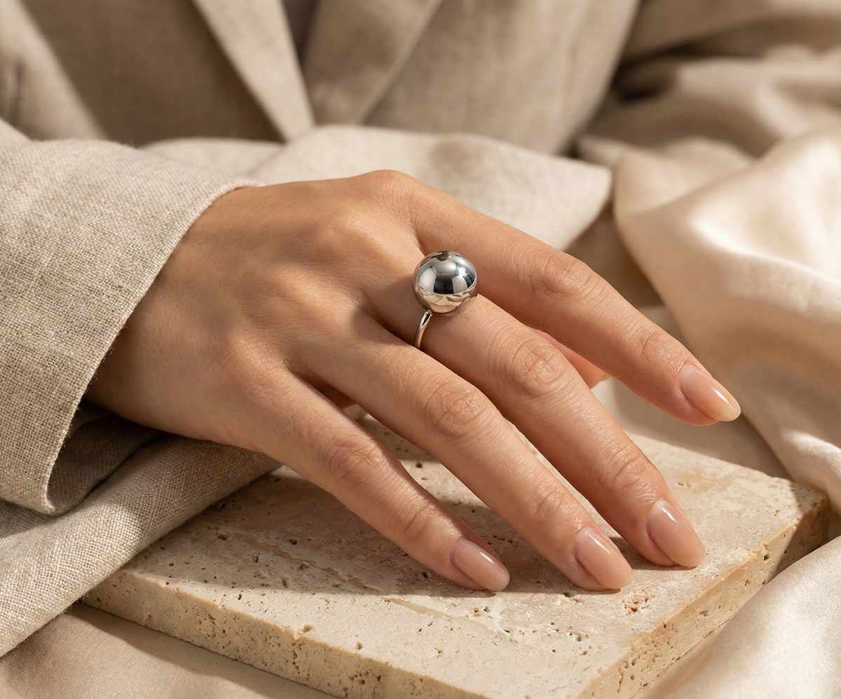 Main portant une bague en acier inoxydable argenté en forme de boule pour femme