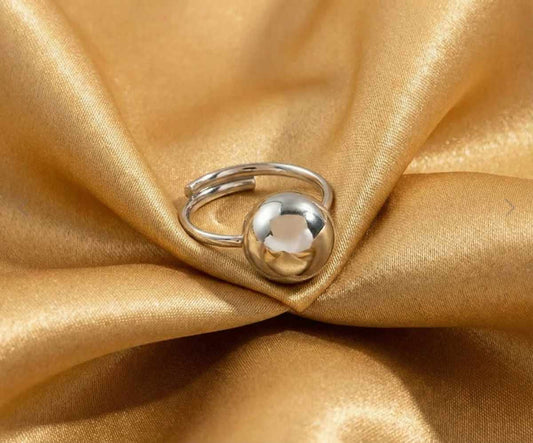 Bague en argent boule pour femme posé sur un tissu satin doré